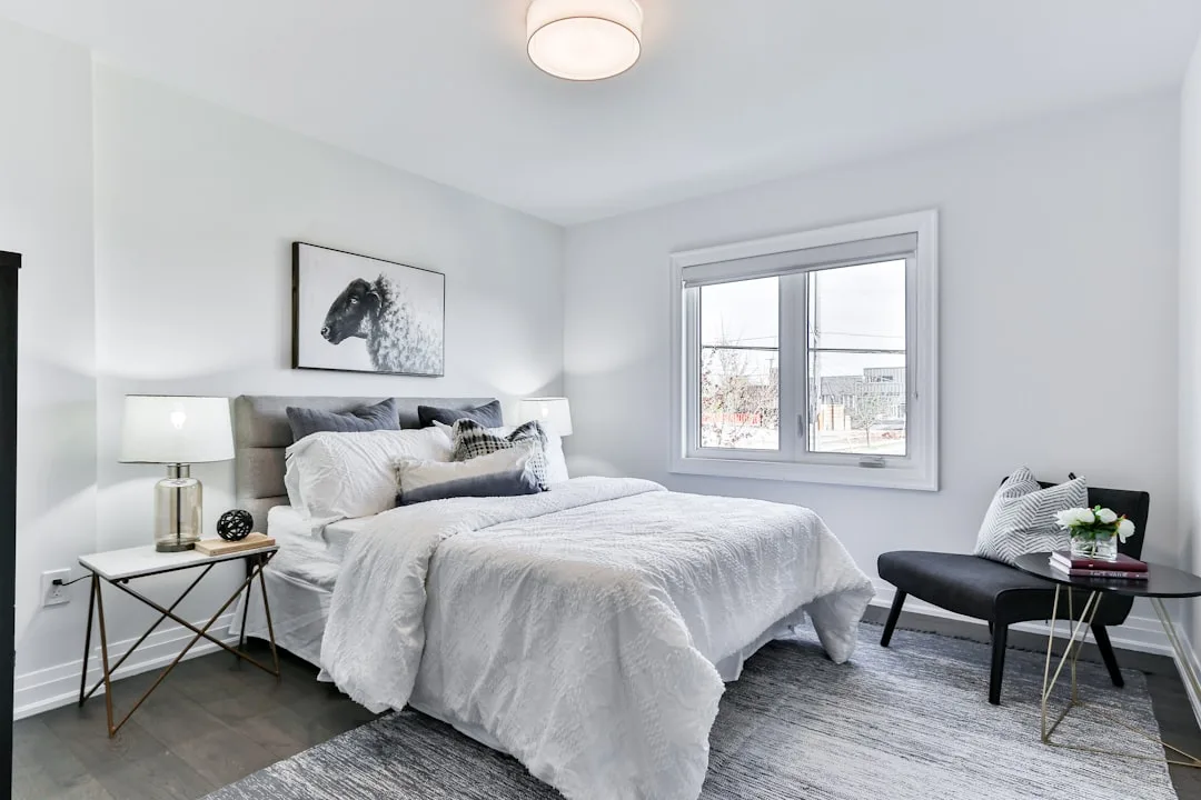 Modern bedroom with mixed gray and white furniture tones, upholstered headboard, black chair and gold accent side tables