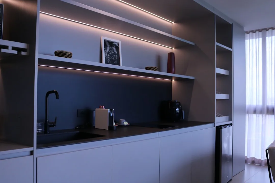 Modern kitchen with LED strip smart lighting under shelves illuminating dark backsplash and white cabinetry