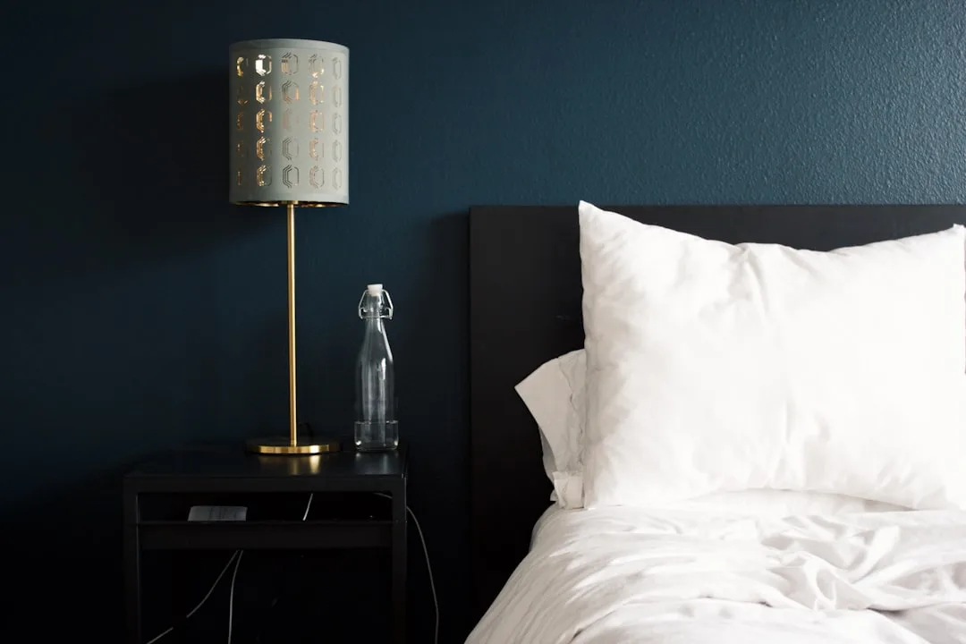 Dark teal bedroom wall with black headboard, white bedding, and gold accent lamp on nightstand