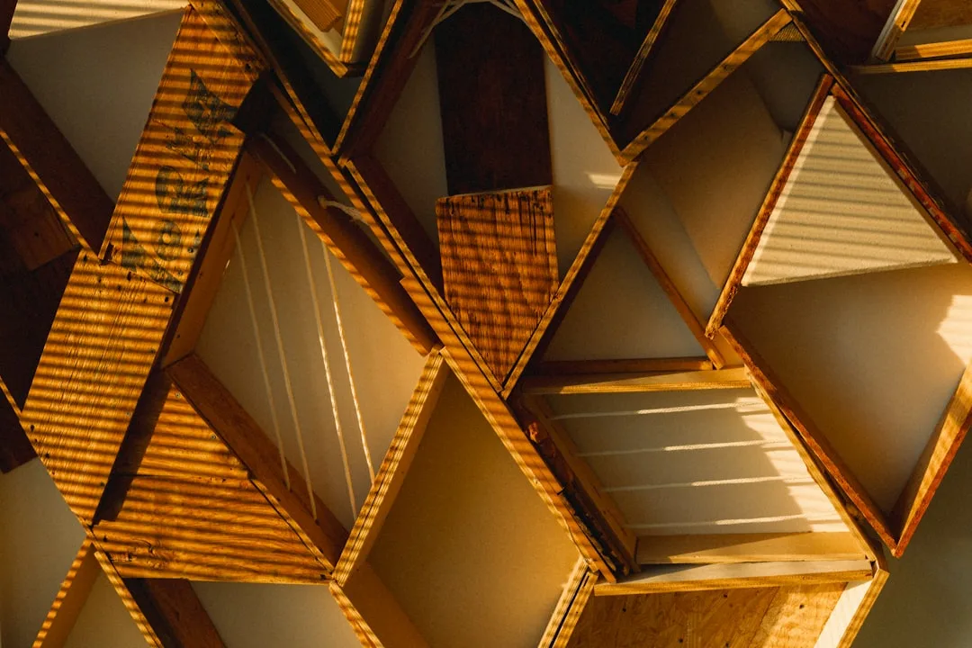 Diamond-shaped triangular wooden shelving unit with warm golden light casting geometric shadows on storage compartments