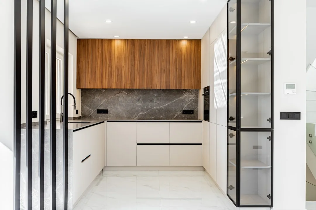 Modern galley-style kitchen with white handleless cabinets, walnut upper cabinetry, dark marble backsplash and U-shaped 