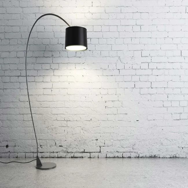 Modern arc floor lamp with black cylindrical shade and curved metal stem against white painted brick wall