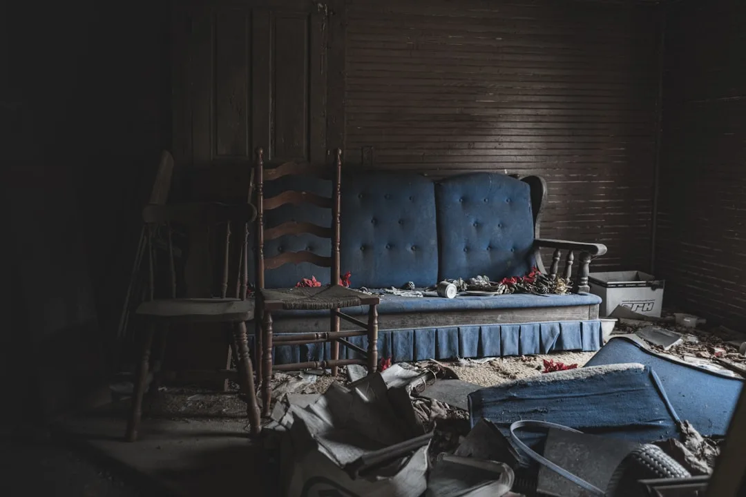 Abandoned room with misplaced blue tufted sofa and wooden chairs surrounded by debris illustrating poor furniture placem