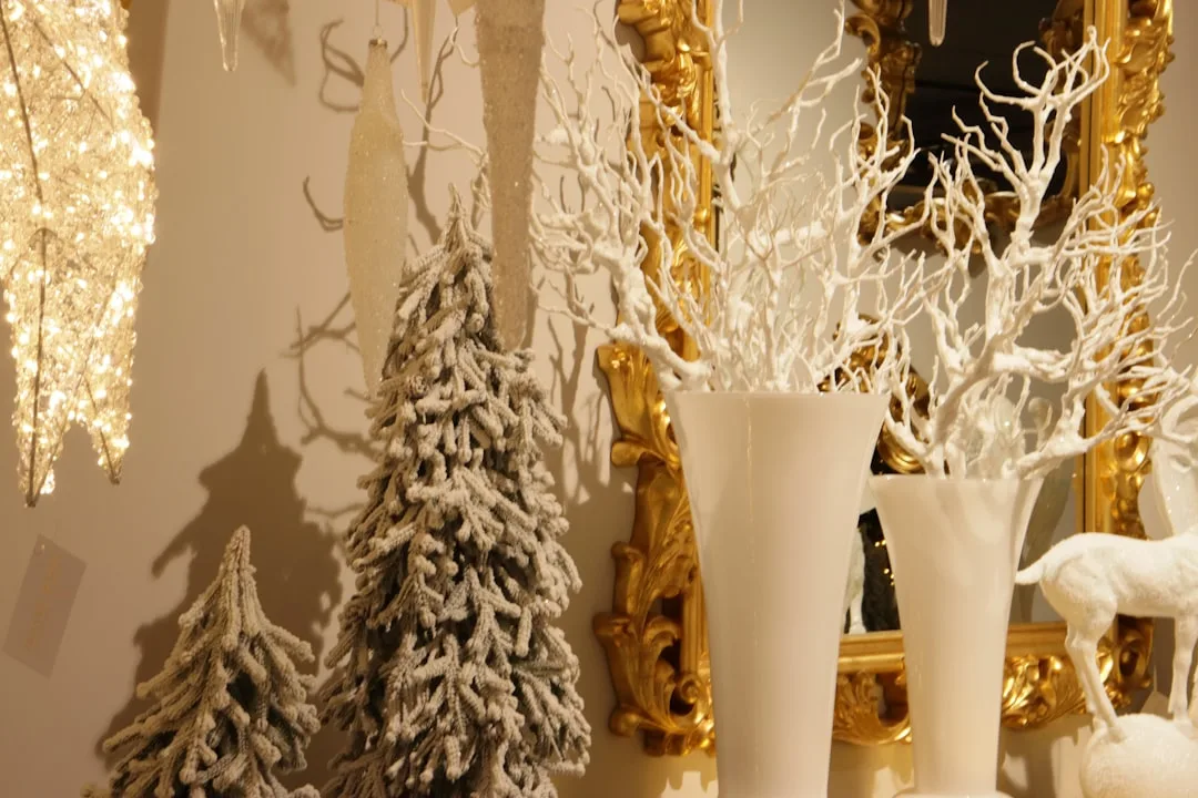 White flocked Christmas trees and white branch vases styled on a console table with gold ornate mirror