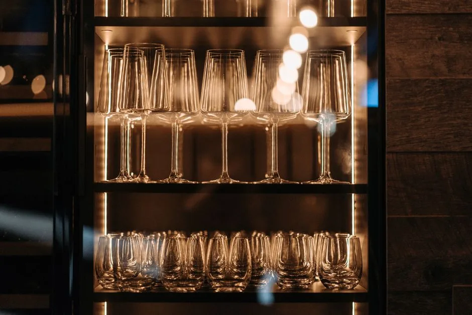 Backlit bar shelves organized with wine glasses on top row and stemless glasses on bottom row in depth zones