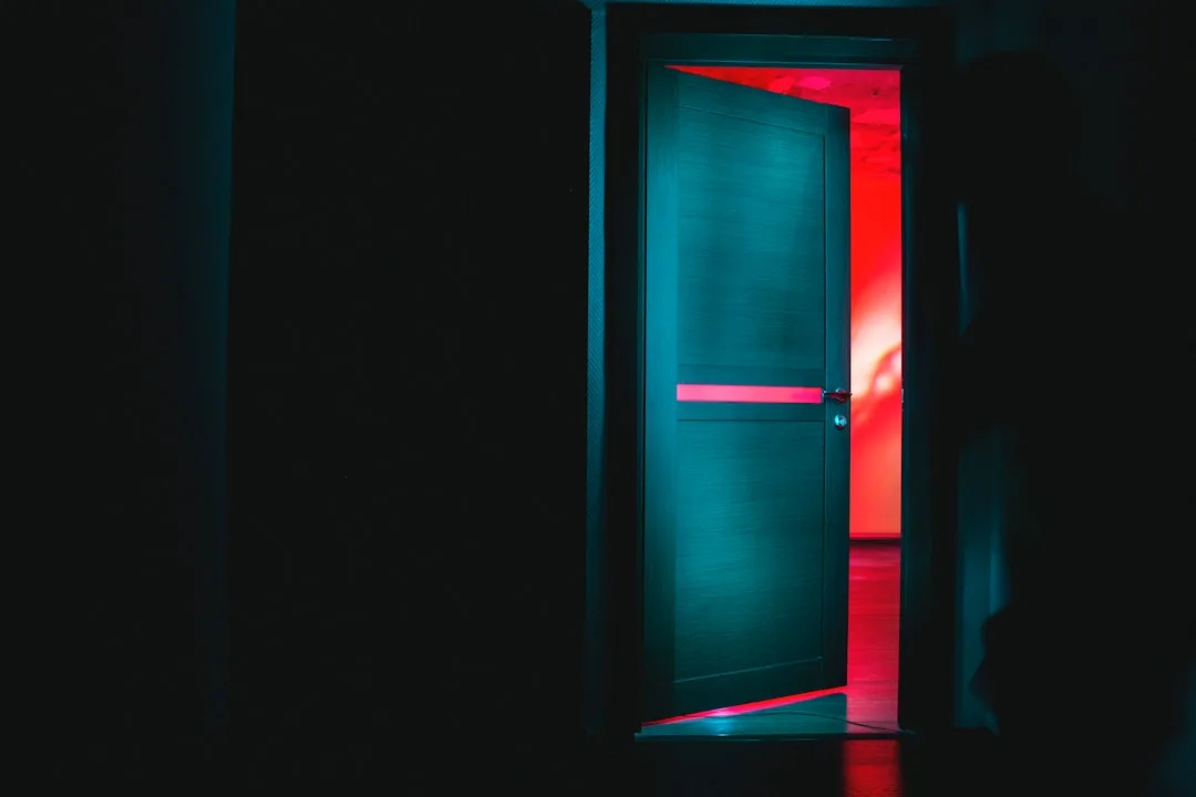 Ajar interior door with dramatic red neon light glowing through the opening in a dark room