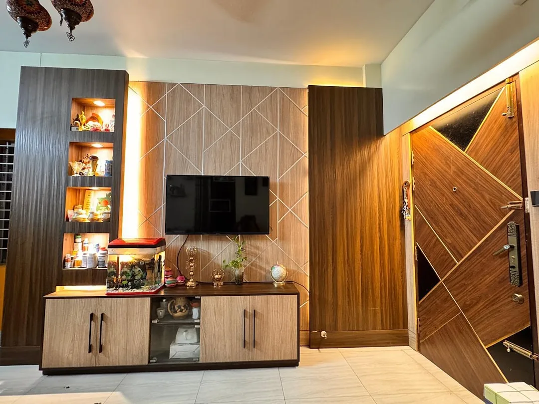 Wooden main entrance door with geometric panel design next to built-in TV wall unit with display shelves in modern livin