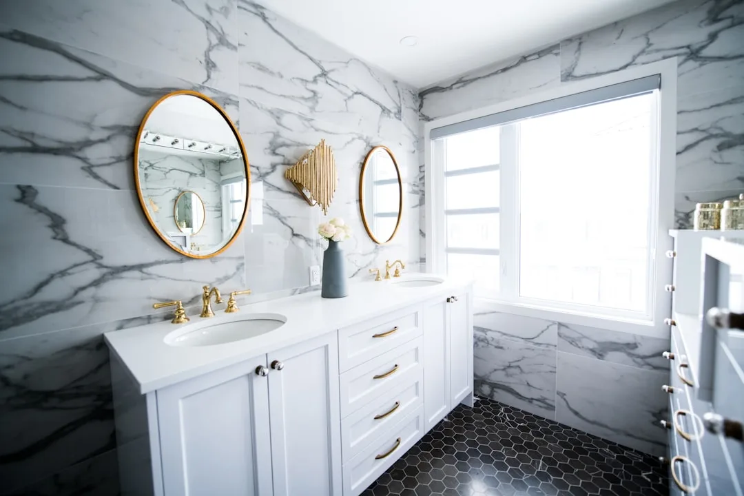 Luxury bathroom with white marble walls, black hexagon floor tiles, double vanity and gold fixtures showing tile layout 
