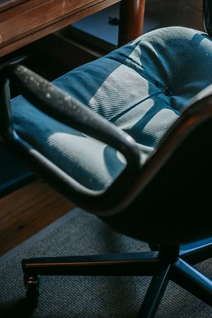 Vintage office chair with blue fabric upholstery tucked under a wooden desk in a home office setup