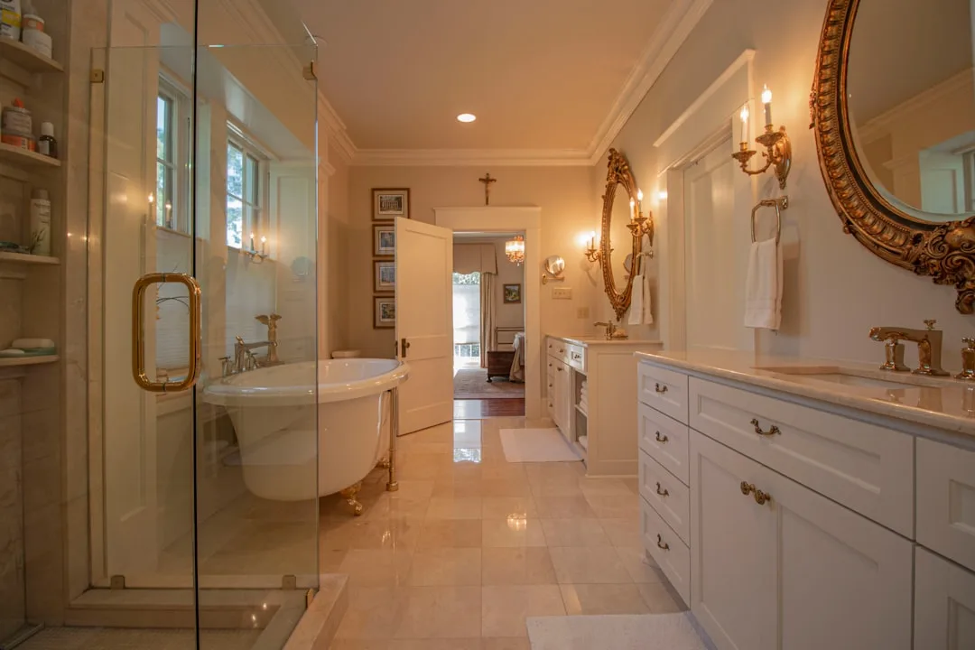 Luxury master bathroom with clawfoot tub, glass shower, dual vanity, and ornate gold mirrors connecting to bedroom suite