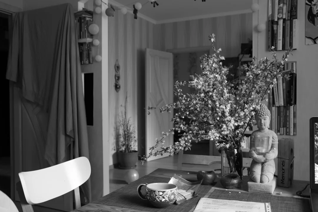 Styled dining table foreground with Buddha statue, flowering branches, ceramic mug and personal objects in cozy home int