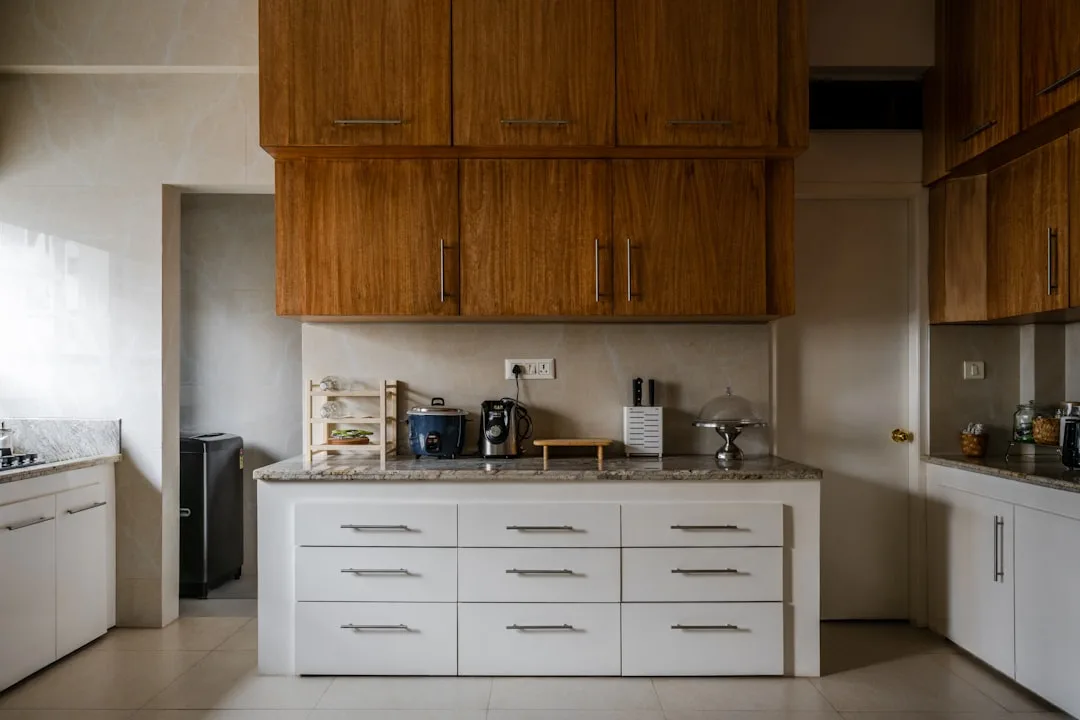 Modern kitchen with wood upper cabinets, white drawer base unit, marble countertop, and small appliances organized by zo