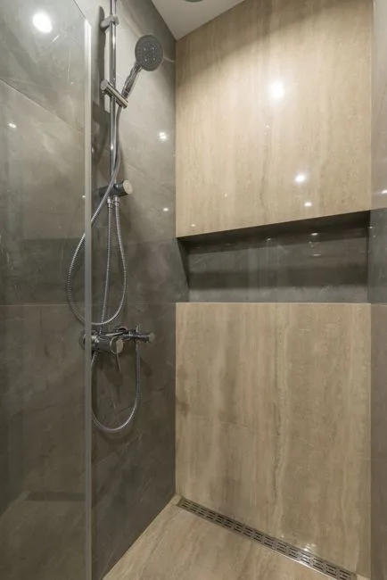 Compact wet room shower with linear drain, marble-effect tiles and built-in niche shelf showing efficient small space de
