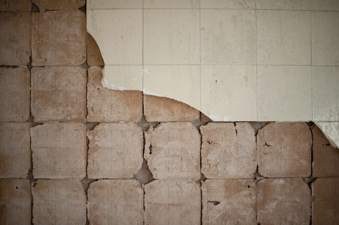 Deteriorating wall tiles with surface coating peeling away revealing rough concrete substrate underneath