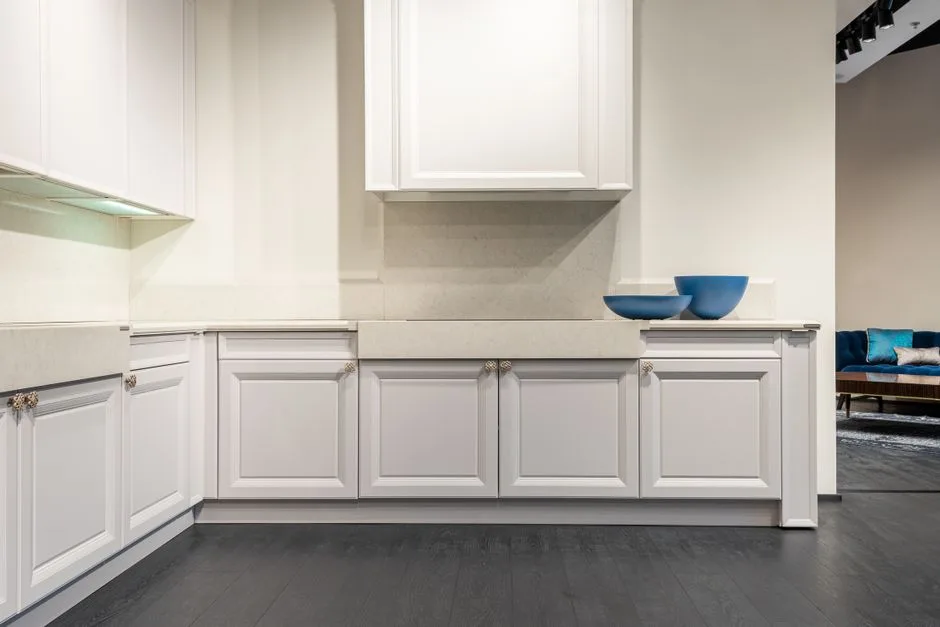 White classic kitchen cabinets with corner layout showing L-shaped base units and marble countertop in modern showroom