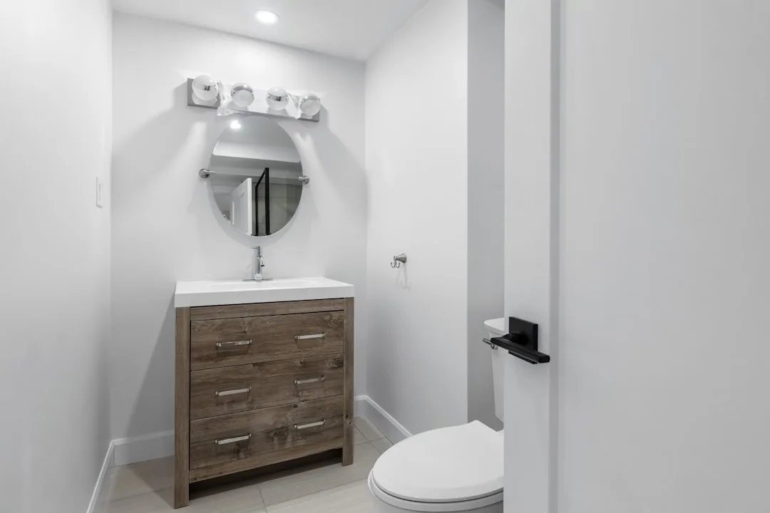 Small powder room with wooden vanity, round mirror