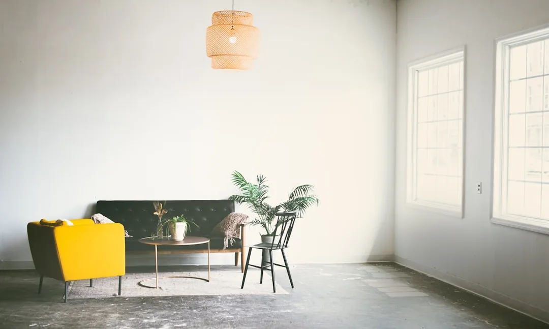 Minimalist living room with warm wicker pendant light, yellow armchair, and white walls showing natural and artificial l