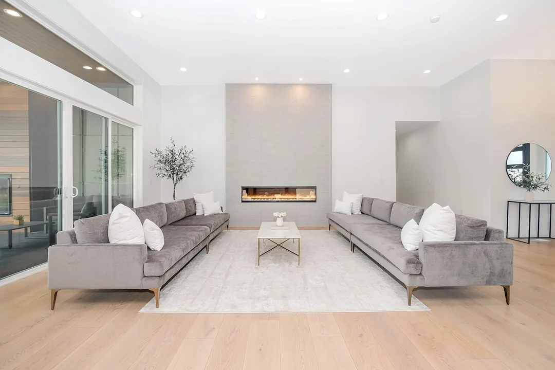Modern living room with greige walls and fireplace surround, gray velvet sofas, light wood floors and white ceiling