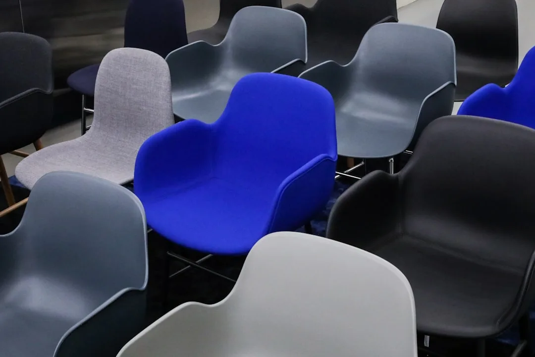 Collection of modern shell chairs in gray, blue, and black arranged closely together showing varied seating styles