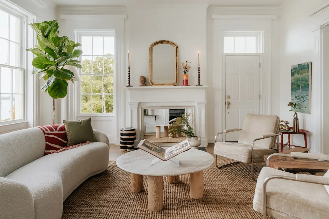 Bright white living room with warm white walls, natural light from large windows, and mixed neutral furnishings showing 