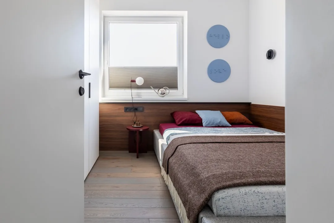 Modern bedroom with low-profile bed frame, wooden headboard, and visible under-bed storage space on light hardwood floor