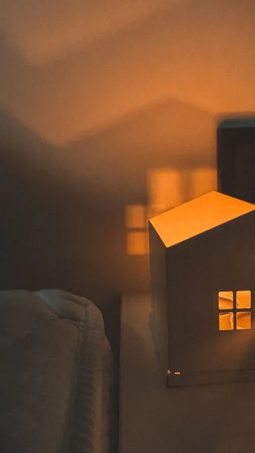 Glowing miniature house lamp casting warm orange light on bedside table in cozy bedroom sleep zone