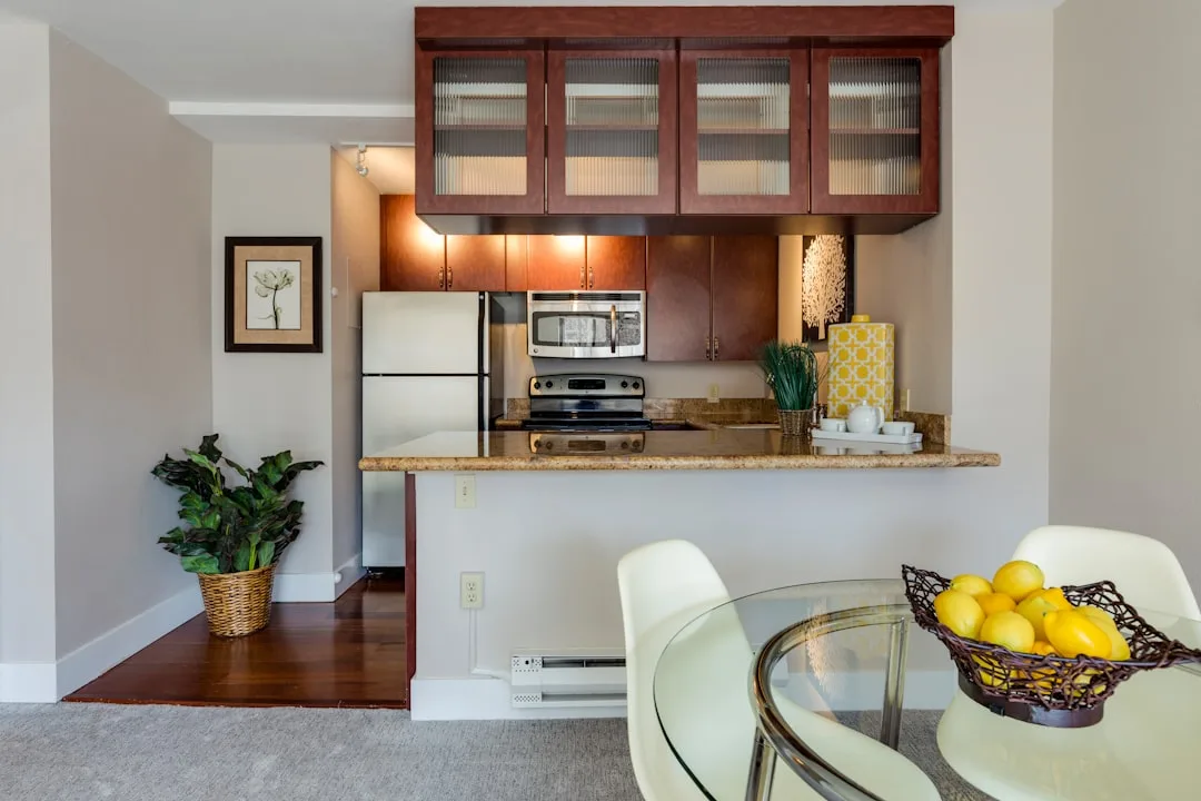 Small kitchen dining combo with glass table, white chairs, granite breakfast bar, and dark wood cabinets in apartment