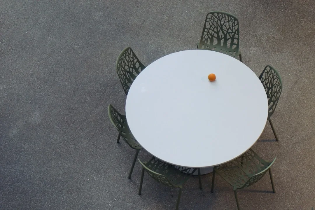 Overhead view of white round outdoor table with green decorative metal chairs and single orange on tabletop