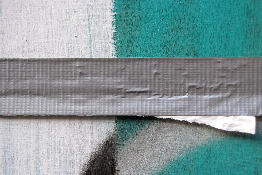 Painter's tape applied on two-tone teal and white painted wall showing tape removal edge and surface texture