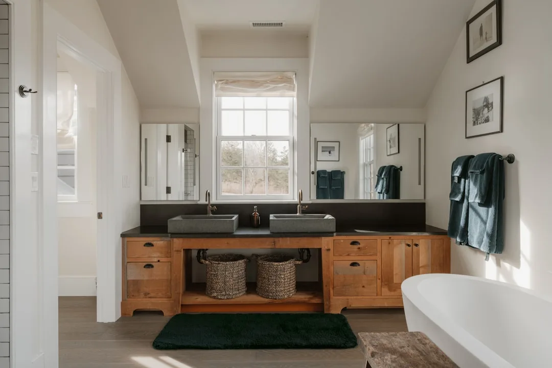 Double vanity master bathroom with wooden cabinets, stone vessel sinks, dark countertop, and freestanding soaking tub