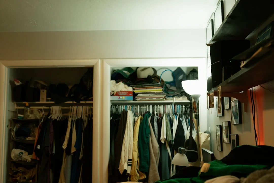 Cluttered reach-in closet showing three vertical zones with hanging clothes, packed shelves, and overhead storage