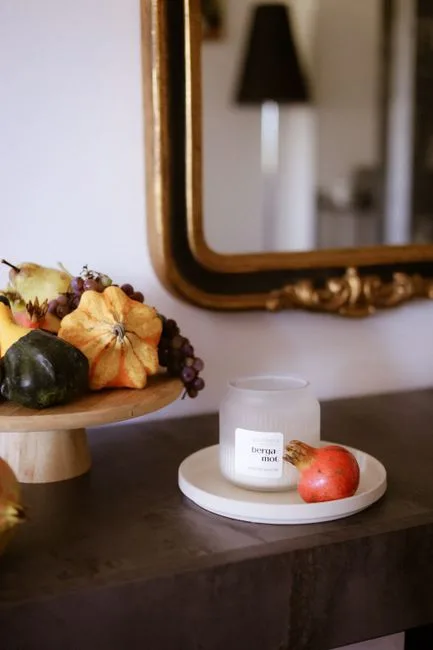 Fall entry table decor with gourds, grapes, pomegranate, and bergamot candle on console table with gold mirror