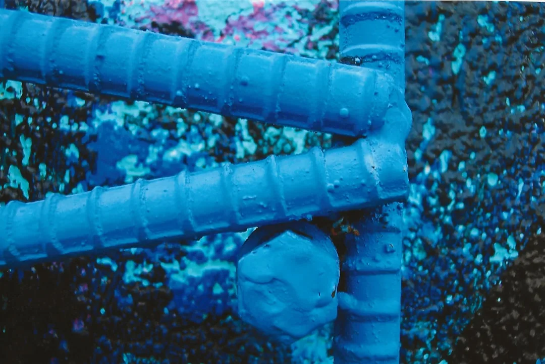 Blue-painted steel rebar joints with water droplets showing waterproofing and structural wet room construction details