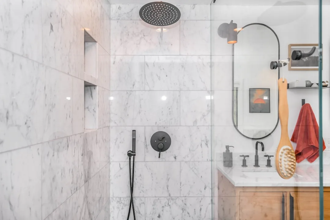 Luxury walk-in shower with marble tiles, matte black rainfall showerhead and fixtures, glass enclosure and built-in nich