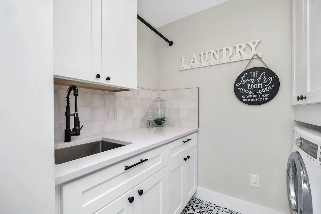 White shaker cabinet laundry room with black faucet sink, tile backsplash, and washer in galley layout