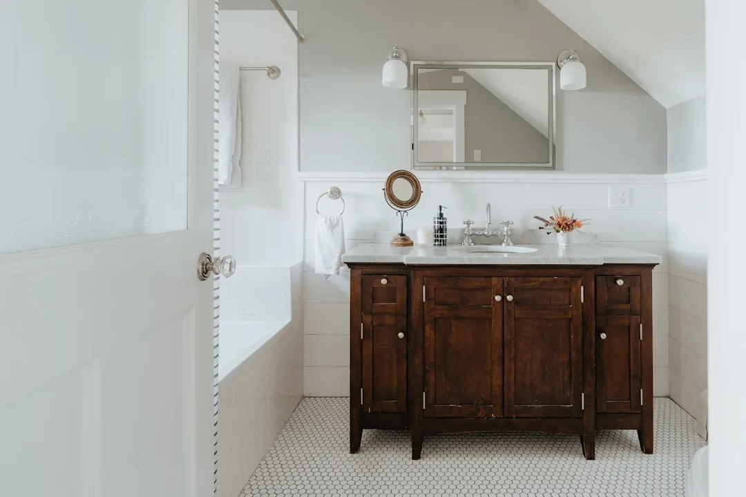 Small bathroom with dark wood vanity cabinet, marble countertop, and under-sink storage in white tiled bathroom