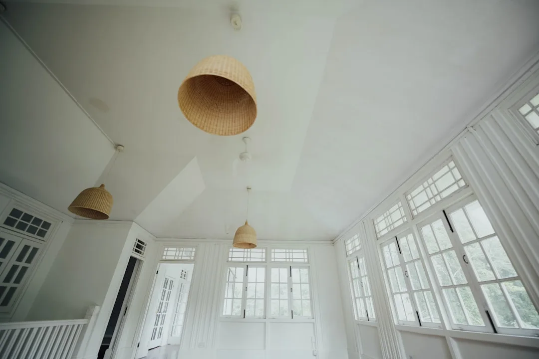 White room with low vaulted ceiling featuring hanging rattan pendant lights and large white-framed windows