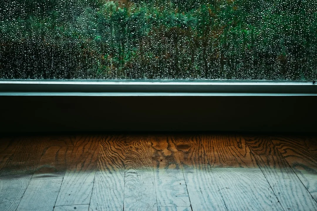 Rain-covered window with condensation above wet wooden floor showing moisture damage disadvantages of wet rooms