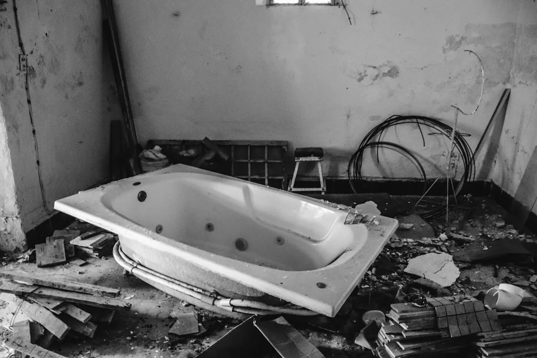 Abandoned freestanding jetted bathtub sitting on debris in a derelict room with peeling walls and construction waste