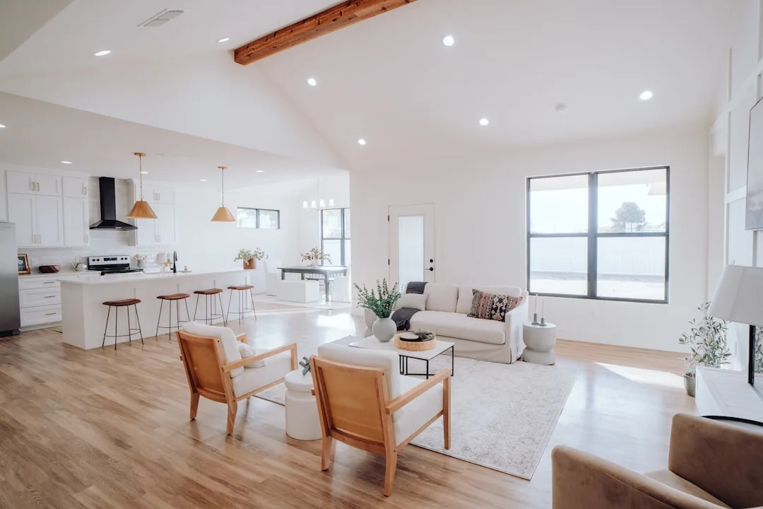 Bright open-plan living room and kitchen with white walls, wood floors, and natural light from north-facing windows
