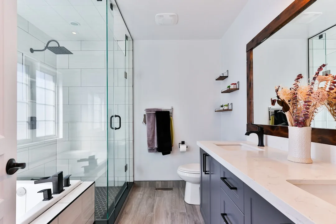 Modern $10000 bathroom remodel with glass shower enclosure, gray vanity, quartz countertop and wood-framed mirror