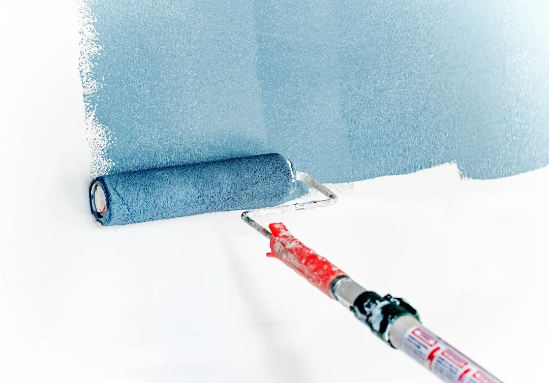 Paint roller applying light blue paint on white wa