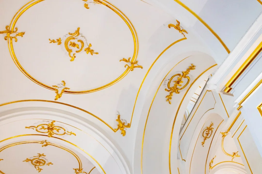 Ornate white ceiling with gold gilded Baroque moldings and circular decorative motifs in a grand interior