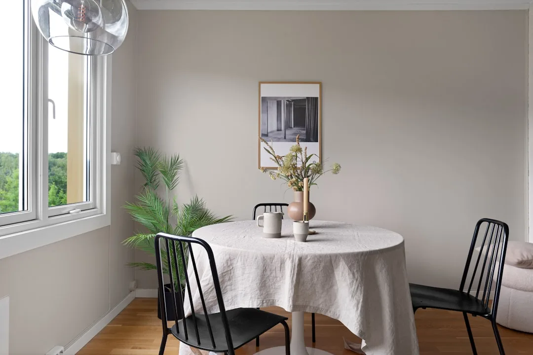 Scandinavian dining room with greige walls, round table with linen cloth, black chairs and natural decor accents