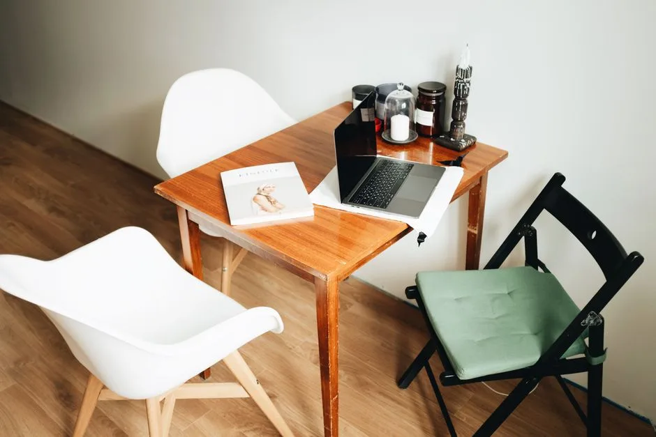 Small wooden drop-leaf style table with laptop and books in a compact living space with two chairs