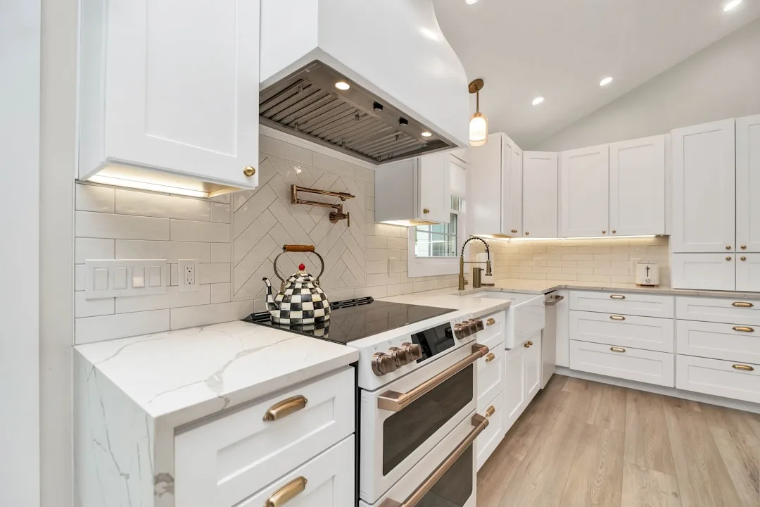 White kitchen with LED under-cabinet lighting illuminating marble countertops and shaker cabinets with gold hardware