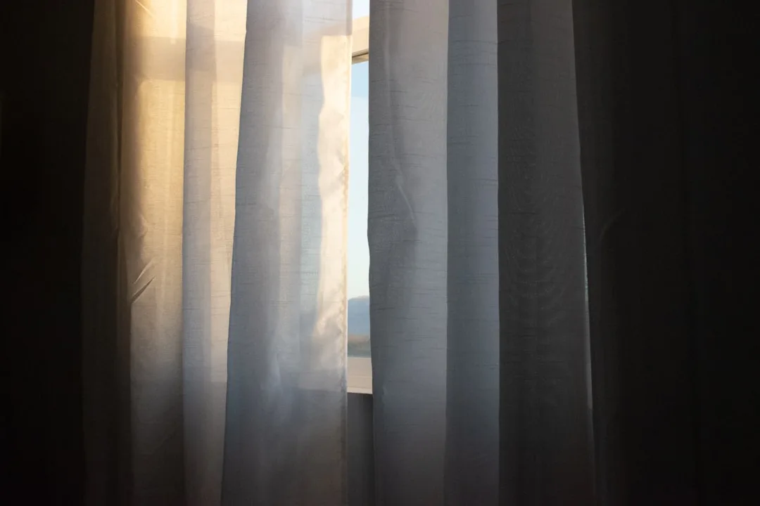 Sheer curtains filtering warm natural sunlight through a window with a mountain view, demonstrating light control for ho
