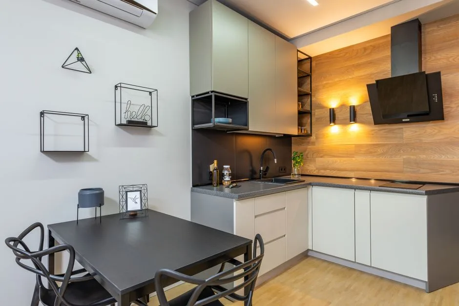 Small kitchen dining area with dark rectangular table and black chairs next to modern L-shaped kitchen with green cabine