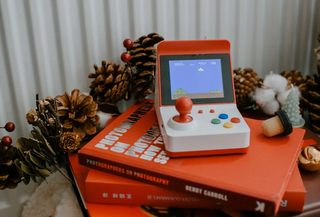 Red and white mini arcade console displaying Super Mario Bros on books surrounded by pine cones and Christmas holiday de