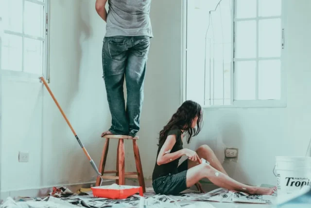 Couple renovating a room, one standing on a stool